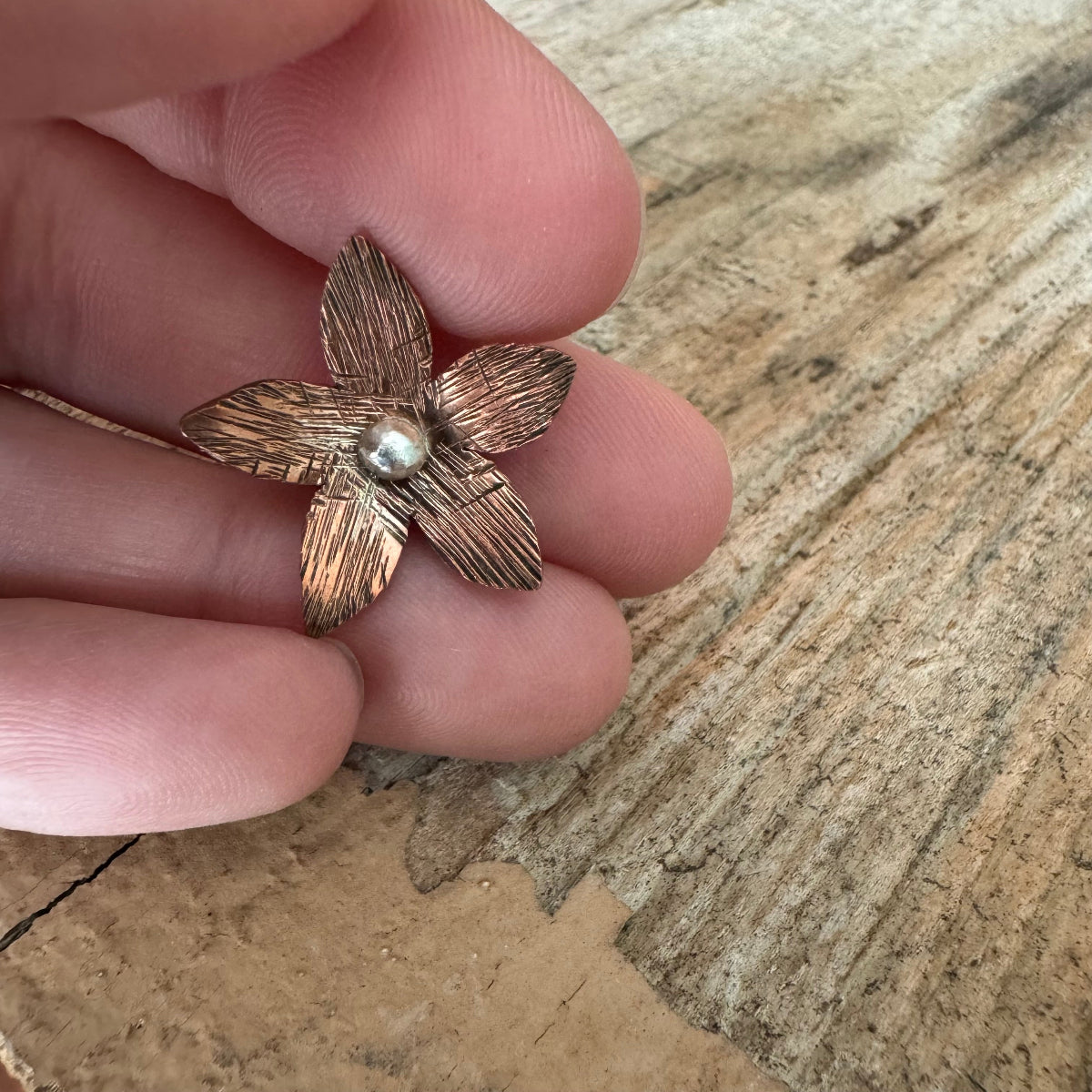Luella handmade copper and sterling silver floret held in hand, showcasing detailed craftsmanship and size before custom band design