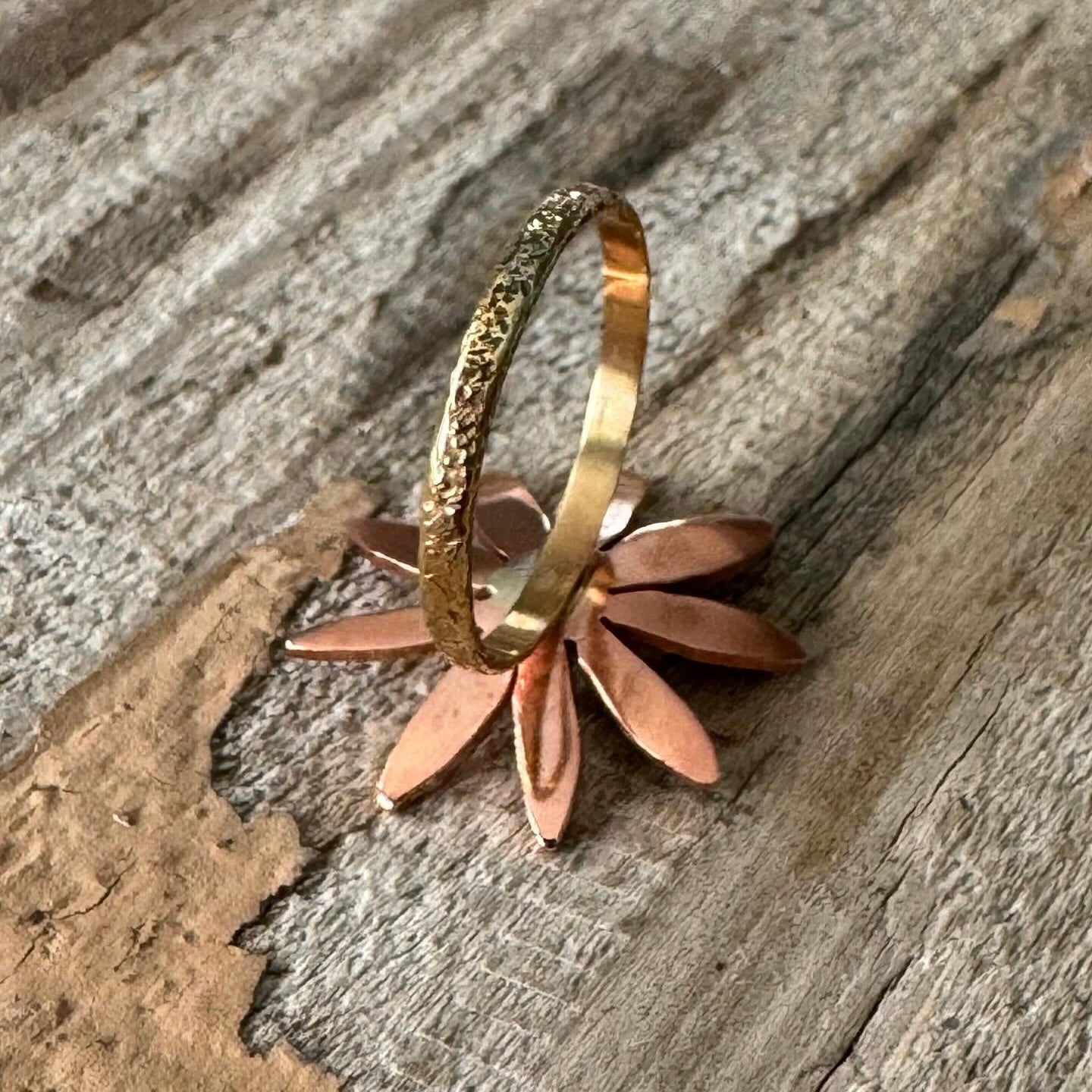 Close-up of handcrafted copper and sterling silver flower ring with textured brass ring band

