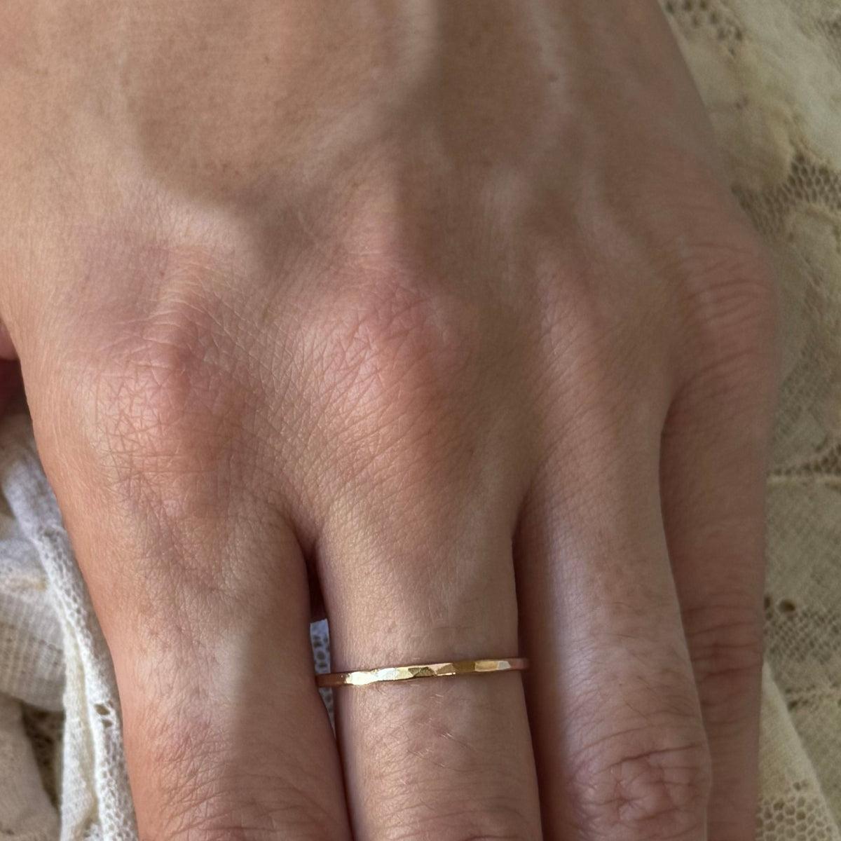 Woman's hand wearing a gold-filled and hammered stacking ring on lace background
