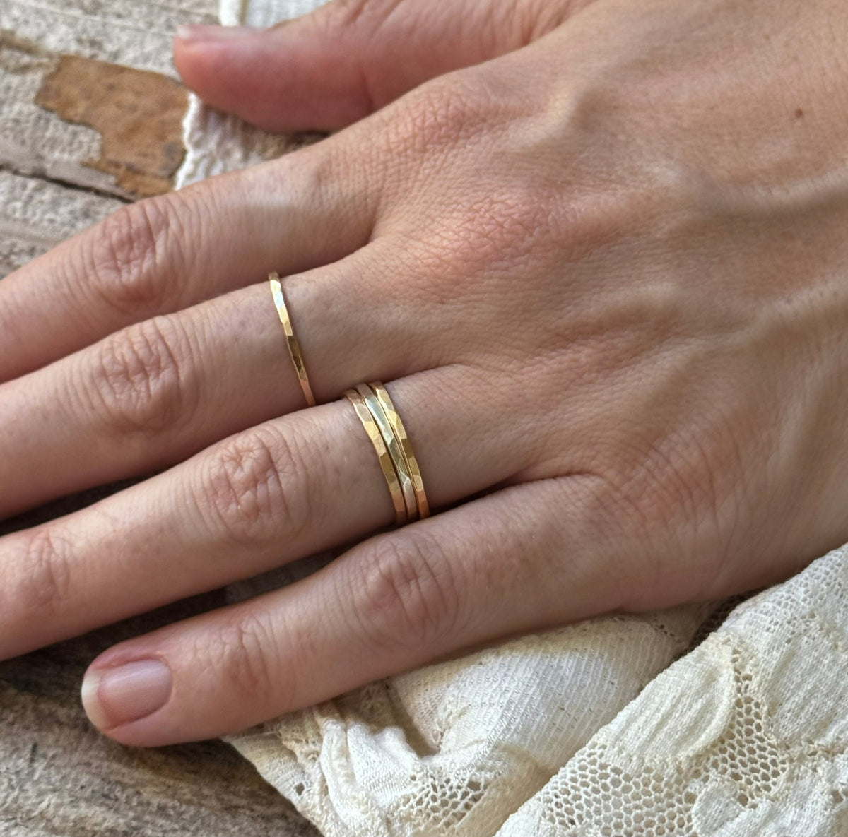 woman's hand wearing 4 gold and silver rings with lace and wood background
