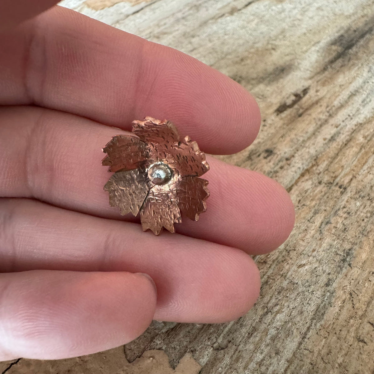 Nelly handcrafted copper and sterling silver floret resting in hand, highlighting artisan detail and scale before custom ring band is made