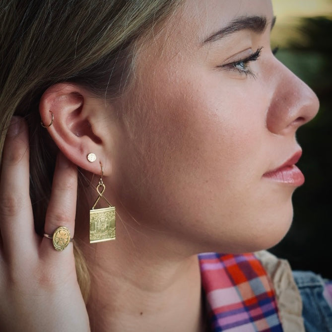 Close-up of a woman wearing brass victorian inspired earrings with a blurred background