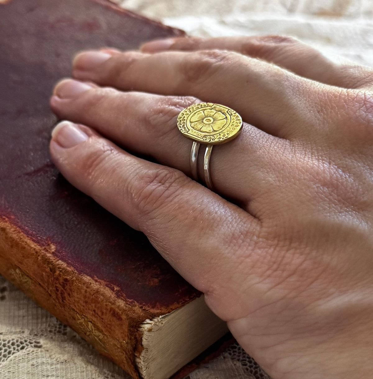Woman wearing rings with hand resting on burgundy book with lace background
