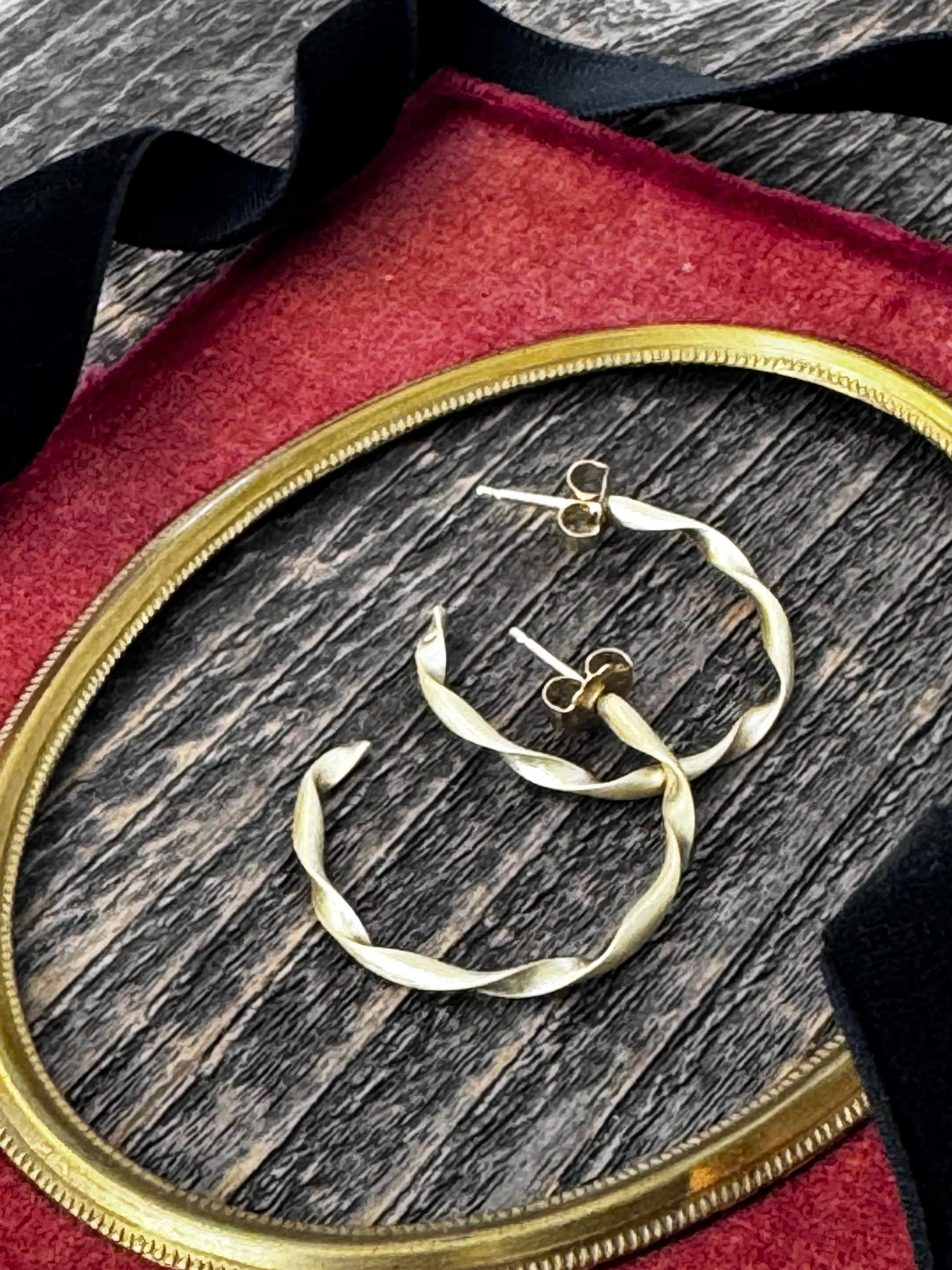 Brass hoop earrings on a wooden surface with a red velvet background