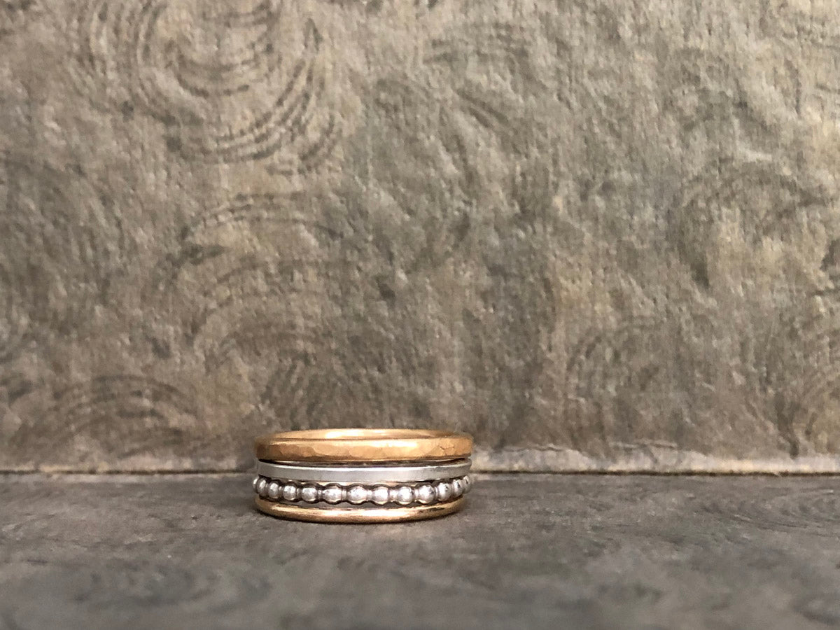 Mixed metal stacking rings—Alpine Loop set stacked together with a gray vintage background, showcasing hammered brass, beaded silver, and gold-filled bands by Narrow-Gauge Designs
