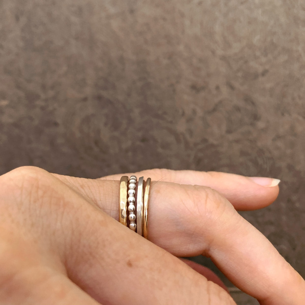 Side profile of Alpine Loop stacking ring set worn on a finger—mixed metal bands including hammered brass, beaded silver, square sterling silver, and gold-filled ring, handcrafted by Narrow-Gauge Designs