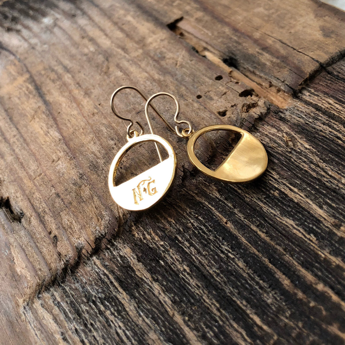 Billy the Kid gold minimalist earrings resting on weathered wooden surface, highlighting their smooth gold discs and handcrafted details.