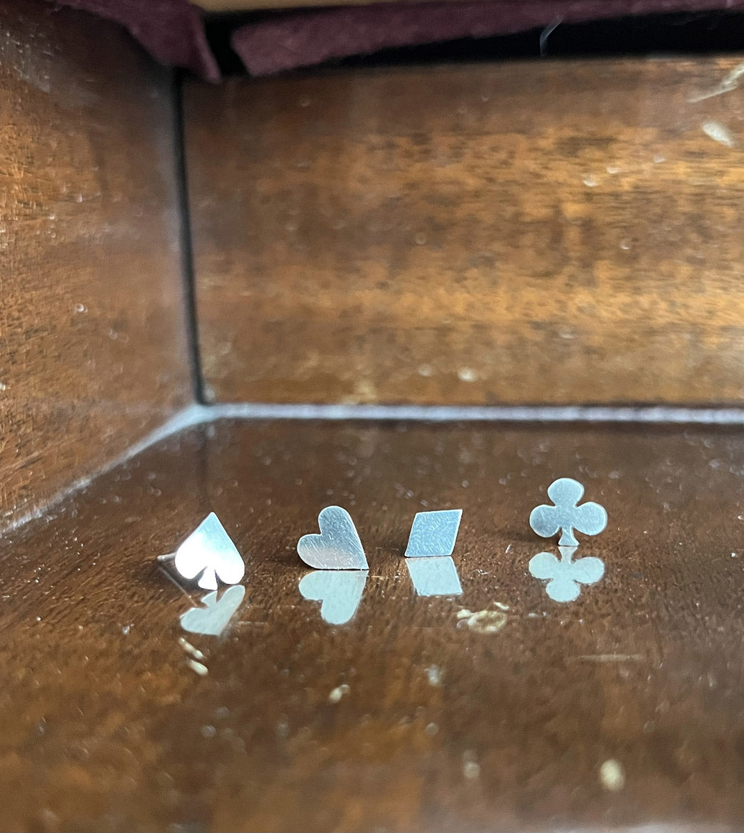 Close-up of all four Pharo sterling silver stud earrings—club, spade, diamond, and heart—resting on a weathered wooden piano surface, showcasing their polished details and craftsmanship.