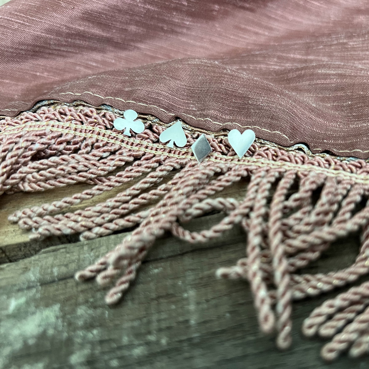 Pharo sterling silver card suit earrings—Heart, Spade, Club, and Diamond—nestled on a mauve fringed tablecloth.
