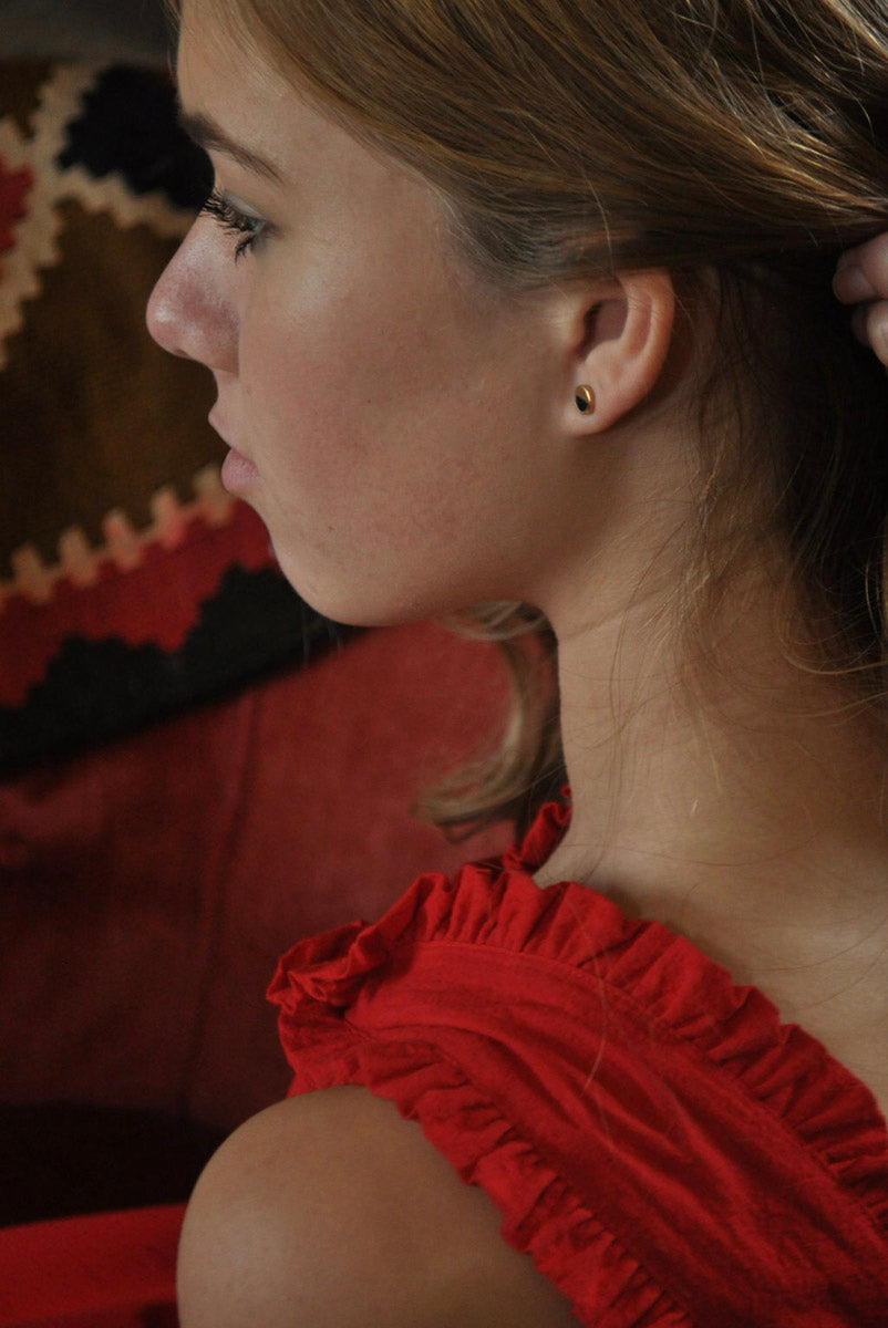 Profile shot of a model in a red dress wearing one Holliday stud earring, capturing the gold finish and Black Jade detail against her ear.